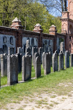 Foto de Lodz, Polonia - 4 de mayo de 2023: Cementerio judío de Lodz, lápidas y fosas comunes de las víctimas del gueto de Lodz. Lapidarium y la pared de ladrillo rojo que rodea la necrópolis - Imagen libre de derechos