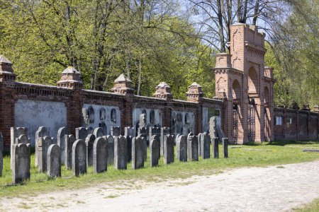 Foto de Lodz, Polonia - 4 de mayo de 2023: Cementerio judío de Lodz, lápidas y fosas comunes de las víctimas del gueto de Lodz. Lapidarium y la pared de ladrillo rojo con puerta interna - Imagen libre de derechos