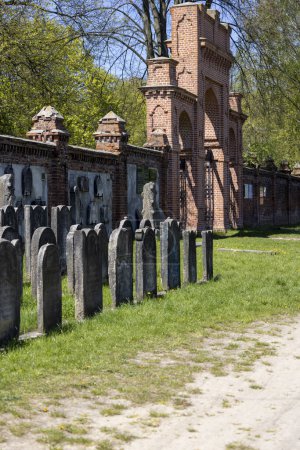 Foto de Lodz, Polonia - 4 de mayo de 2023: Cementerio judío de Lodz, lápidas y fosas comunes de las víctimas del gueto de Lodz. Lapidarium y la pared de ladrillo rojo con puerta interna - Imagen libre de derechos