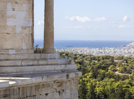 Photo for Temple of Athena Nike at Propylaia, monumental ceremonial gateway to the Acropolis of Athens, Greece. In the distance, aerial view of the city and sea with port of Piraeus - Royalty Free Image