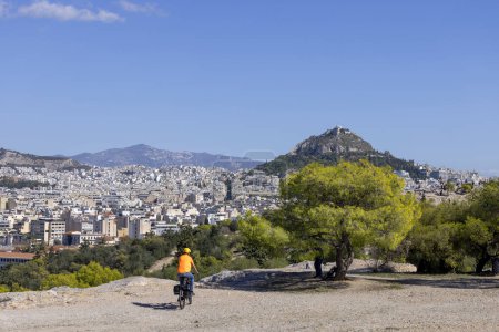 Téléchargez les photos : Vue de la colline de Mouseion de la ville et du mont Lycabettus sur un fond de ciel bleu, Athènes, Grèce. Au premier plan un cycliste - en image libre de droit