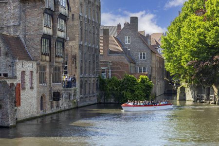 Foto de Brujas, Bélgica - 19 de mayo de 2023: Vista desde Mariabrug (Puente de María) de Rosary Quay (Rozenhoedkaai) por el canal de agua Dijver Canal. Turistas en un barco durante un crucero por los canales de la ciudad - Imagen libre de derechos