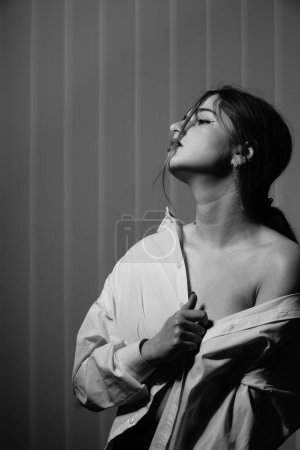 Foto de Foto en blanco y negro de una hermosa joven con una sola camisa blanca sobre su cuerpo desnudo posando en un estudio - Imagen libre de derechos
