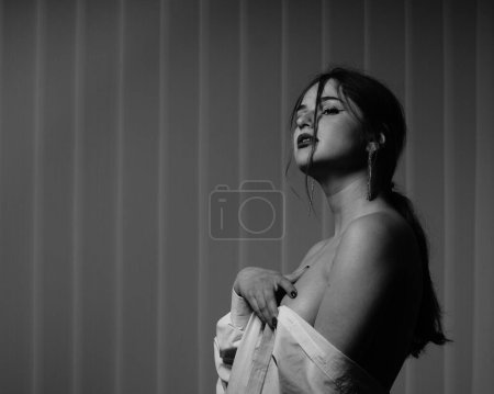 Photo for Black and white photo of a beautiful young girl in only one white shirt over her naked body posing in a studio - Royalty Free Image