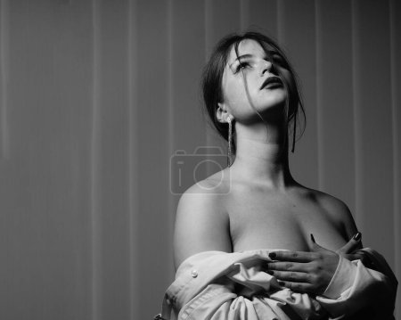 Foto de Foto en blanco y negro de una hermosa joven con una sola camisa blanca sobre su cuerpo desnudo posando en un estudio - Imagen libre de derechos