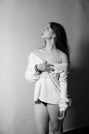 Photo for Black and white photo of a beautiful young girl in only one white shirt over her naked body posing in a studio - Royalty Free Image