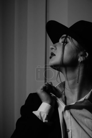 Photo for Black and white photo of a beautiful young girl in only one black blazer and hat posing in a studio - Royalty Free Image