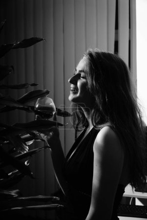 Photo for Black and white photo of a beautiful sensual woman in a black dress with a glass of whiskey posing for the camera - Royalty Free Image