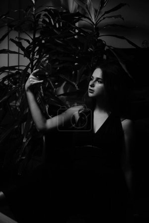 Téléchargez les photos : Photo noir et blanc d'une belle femme sensuelle dans une robe noire avec un verre de whisky posant pour l'appareil photo - en image libre de droit