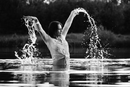 Foto de Foto en blanco y negro de una chica bailando en un lago en el parque. pelo y ropa húmedos. - Imagen libre de derechos
