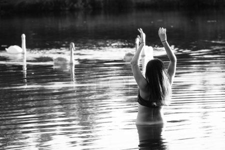Téléchargez les photos : Photo en noir et blanc d'une fille avec des oiseaux sur un lac dans le parc. cheveux et vêtements mouillés. - en image libre de droit