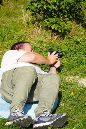 Téléchargez les photos : Man with a camera lying on the grass - en image libre de droit
