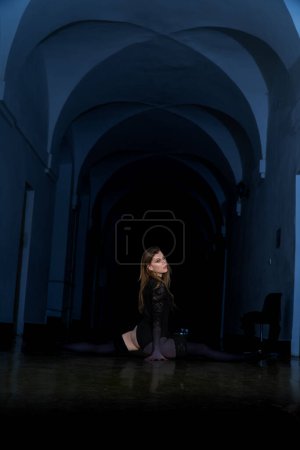 Foto de Hermosa chica en un vestido negro hizo las divisiones en la habitación oscura - Imagen libre de derechos