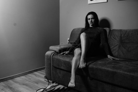 Foto de Foto en blanco y negro de una buena mujer en un vestido corto a rayas sentado en el sofá de la habitación - Imagen libre de derechos