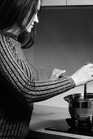 Téléchargez les photos : Photo noir et blanc d'une belle femme cuisinière dans la cuisine - en image libre de droit