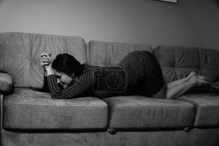 Téléchargez les photos : Photo noir et blanc d'une jolie femme dans une robe courte rayée couchée sur le canapé dans la chambre - en image libre de droit