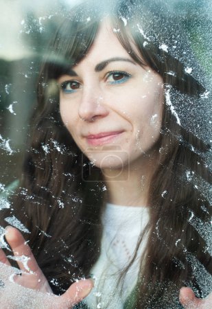 Photo for Young woman is looking throught the snowy window - Royalty Free Image
