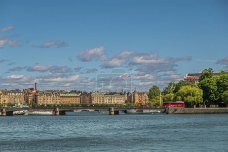 Téléchargez les photos : Suède, Stockholm - 17 juillet 2022 : Skeppholmsbron pont à partir de Skeppsbron quay. sous nuage bleu et paysage urbain derrière. Bus public rouge et feuillage vert - en image libre de droit