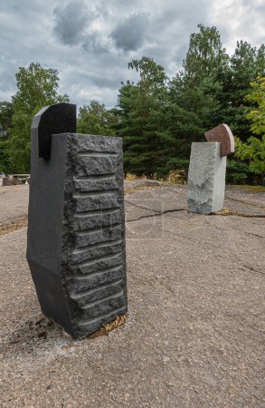 Photo for Finland, Kotka - July 18, 2022: Sopokanlahti park and lake. Black and gray modern sculpted rock menhirs as art on plateau under gray cloudscape. Green belt as backdrop. - Royalty Free Image