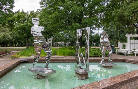 Foto de Finlandia, Kotka - 18 de julio de 2022: Parque Sopokanlahti y lago. Figuras femeninas y masculinas de metal brillante recortan estatuas de arte en la piscina de agua verde. Correa verde como telón de fondo - Imagen libre de derechos