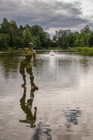 Photo for Finland, Kotka - July 18, 2022: Sopokanlahti park and lake. Camouflage statue standing on top of water with duck nearby under dark gray cloudscape. Green belt as backdrop - Royalty Free Image