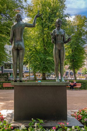 Photo for Helsinki, Finland - July 19, 2022: Back side, Greenish bronze double statue of woman on blavk pedestal in park known as Fact and Fable memorial to Zacharias Topelius. Street sceme on horizon - Royalty Free Image
