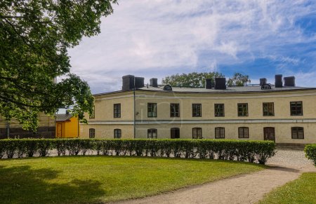 Foto de Helsinki, Finlandia - 19 de julio de 2022: Fortaleza Suomenlinna. Edificio amarillo en la rotonda de la Tumba de Augustin Ehrensvraed bajo un paisaje nublado azul. césped verde y follaje - Imagen libre de derechos