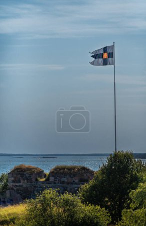 Foto de Helsinki, Finlandia - 20 de julio de 2022: Suomenlinna Fortaleza del mar. Bandera de la fortaleza sobre muralla y follaje verde cerca - Imagen libre de derechos