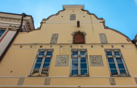 Téléchargez les photos : Estonie, Tallinn - 21 juillet 2022 : Pikk 26, rue est la façade jaune historique de la Maison de la Confrérie des Têtes Noires avec plusieurs sculptures murales en ciment gris entre les fenêtres sous le ciel bleu - en image libre de droit