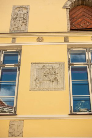 Téléchargez les photos : Estonie, Tallinn - 21 juillet 2022 : Pikk 26, rue est la façade jaune historique de la Maison de la Confrérie des Têtes Noires avec quelques sculptures murales en ciment gris entre les fenêtres montrant cheval et chevalier - en image libre de droit