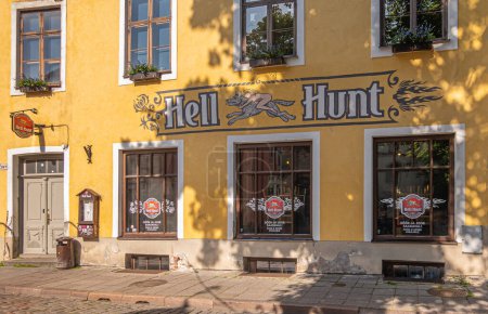 Photo for Estonia, Tallinn - July 21, 2022: Yellow front facade at Hell Hunt pub, bistro and restaurant with colorful logo, 3 large windows and entrance door at Pikk 39 - Royalty Free Image