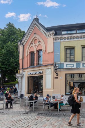 Foto de Estonia, Tallin - 21 de julio de 2022: Fachada y ventana del restaurante McDonalds en la calle Viru con peatones bajo un paisaje azul nublado. Follaje verde - Imagen libre de derechos