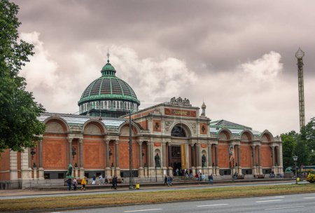 Photo for Copenhagen, Denmark - July 23, 2022: Front red stone facade with arches of historic Ny Carlsberg Glyptotek building with large green framed dome under gray cloudscape. Pdestrians in front - Royalty Free Image
