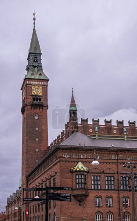 Téléchargez les photos : Copenhague, Danemark - 23 juillet 2022 : Coin nord-ouest de la mairie de briques rouges avec son haut clocher, son horloge dorée et sa flèche verte pointue, contre un paysage nuageux gris sur Radhuspladsen - en image libre de droit