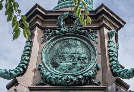 Foto de Copenhague, Dinamarca - 24 de julio de 2022: Ivar Huitfeldt Column detail. Estatua mural de bronce en la parte inferior del barco Almirantes en la columna de piedra marrón en Langelinie Park bajo el cielo azul claro. - Imagen libre de derechos
