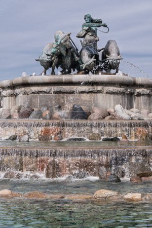 Photo for Copenhagen, Denmark - July 24, 2022: Large bronze statue composition on top of Gefion Fountain featuring oxen and the Norse goddess Gefjon against gray-blue sky. Cascade of waterfalls - Royalty Free Image