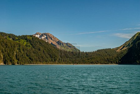 Photo for Resurrection Bay, Alaska, USA - July 22, 2011: Beach with Tonsina cabins. One side the water, other side forest leading up to snow patched brown rock mountain under blue sky - Royalty Free Image