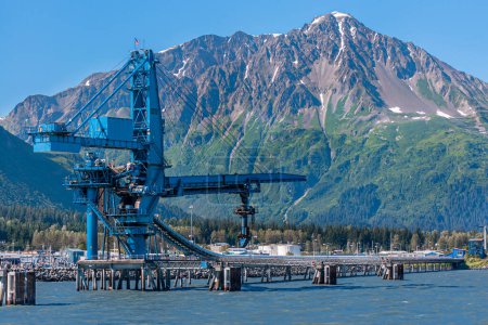 Foto de Seward, Alaska, EE.UU. - 22 de julio de 2011: Primer plano de la correa de transporte de carbón Suneel y la grúa en el muelle rocoso en aguas azules de la Bahía de Resurrección bajo el cielo azul. Cordillera en la espalda - Imagen libre de derechos