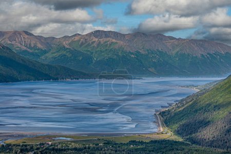 Photo for Girdwood Alaska, USA - July 23, 2011: Blue Turnagain Arm, ocean connection, ends on sandy flatlands at low tide. Green forested mountains as backdrop under blue cloudscape. Road 1 along shore - Royalty Free Image