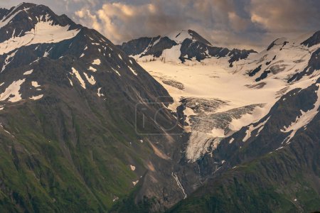Photo for Girdwood Alaska, USA - July 23, 2011: White glacier on top of black rock mountain range in Chugach Park above town. Steep flanks somewhat covered with green vegetation - Royalty Free Image