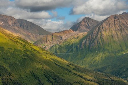 Photo for Girdwood Alaska, USA - July 23, 2011: Different shades of green forested mountains with dry gray rocky tops under blue cloudscape above the settlement - Royalty Free Image