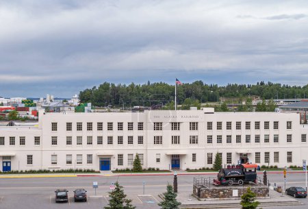 Photo for Anchorage, Alaska, USA - July 23, 2011: Long white stone Alaska Railroad Depot Building with old train engine on display up front. Gray skies and green foliage in back - Royalty Free Image