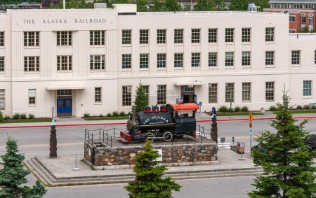 Photo for Anchorage, Alaska, USA - July 23, 2011: Closeup, Long white stone Alaska Railroad Depot Building with old train engine on display up front. Grreen foliage in back - Royalty Free Image