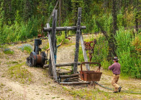Foto de Fox, Alaska, EE.UU. - 26 de julio de 2011: Eldorado Gold Mine museum and park. Antigüedad placer mina eje cable bobinado conjunto de artefactos en la naturaleza verde, pero todavía funciona y demostrado por 2 hombres - Imagen libre de derechos