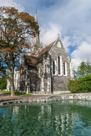 Photo for Copenhagen, Denmark - September 13, 2010: GRay and white stone Saint Albans Church under blue cloudscape with green foliage on both side and partially reflected in green water pond - Royalty Free Image