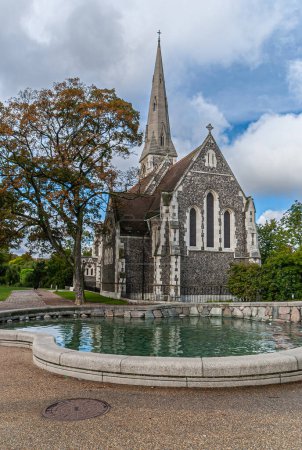 Photo for Copenhagen, Denmark - September 13, 2010: Gray and white stone Saint Albans Church under blue cloudscape with green foliage on both side and green water pond - Royalty Free Image