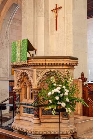 Photo for Copenhagen, Denmark - September 13, 2010: Closeup of beige-brown sculpted Saint Albans Kirke, church, with cross above set against beige pillar. White flowers and green cloth - Royalty Free Image