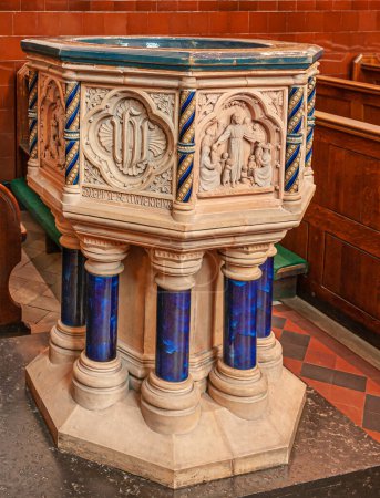 Photo for Copenhagen, Denmark - September 13, 2010: Beige extensively sculpted baptismal font with shiny blue feet set in front of brown prayer benches in St. Albans kirke, church, - Royalty Free Image
