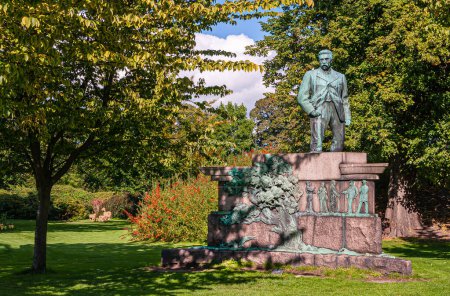 Téléchargez les photos : Copenhague, Danemark - 13 septembre 2010 : Gros plan de Viggo Lauritz Bentheim Statue en bronze Horup sur piédestal en pierre rouge à Kongens Have, Jardin King, entourée de feuillage vert et de fleurs rouges - en image libre de droit