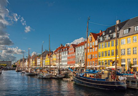 Foto de Copenhague, Dinamarca - 13 de septiembre de 2010: Línea de emblemáticas fachadas de restaurantes Nyhavn en colores brillantes bajo un paisaje azul nublado. Kongens Nyhavn al final, Barcos en el agua del canal - Imagen libre de derechos